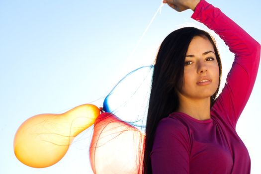 young beautiful woman with balloons into the field against the sky