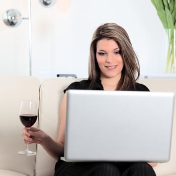 beautiful woman on sofa with computer and glass of red wine
