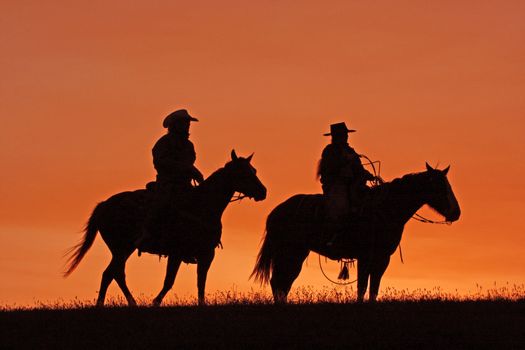 Silhouettes of cowboys on horseback at sunset