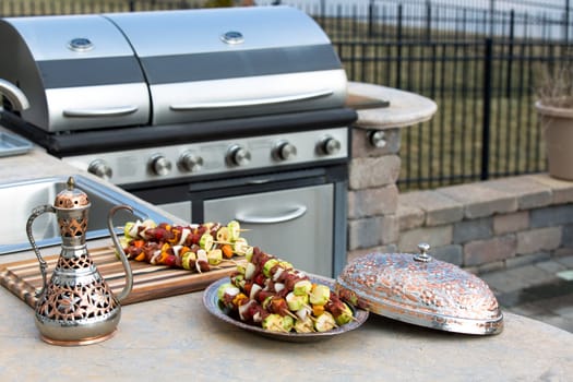 Meat skewers with vegetables at the outdoor kitchen on the concrete counter top. Skewers are in the traditional and authentic looking copper plate with complimenting pitcher.