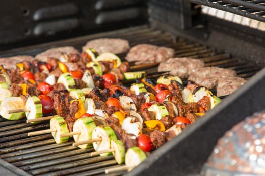 Grilling beef and vegetable  skewers with meat patties on the barbecue.