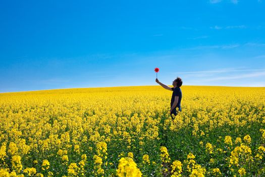 man with pinwheel standing in a field of yellow rape against the blue sky