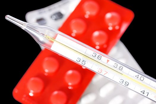 Thermometer and pills on black background