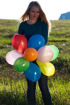 young beautiful woman with balloons into the field against the sky
