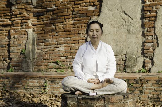 Buddhist woman meditating against ancient temple