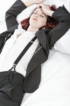 Professional business woman lying on a bed after a long day in the office nursing a headache.
