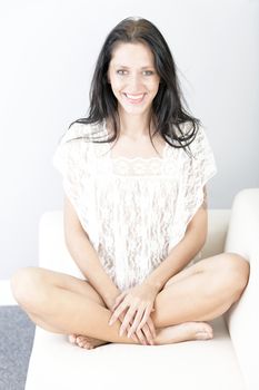 Attractive young woman sitting on a white sofa in casual clothes smiling