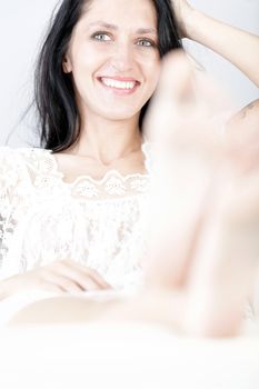 Beautiful young woman with long dark hair lying on her back on a white sofa at home with her feet up