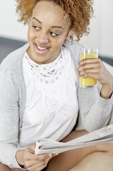 Beautiful young black woman enjoying a newspaper and a glass of juice