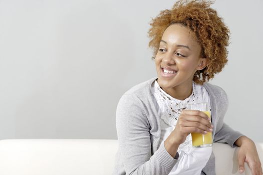 Beautiful young black woman enjoying a glass of fresh juice while sitting on sofa