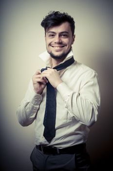 Sexy stylish businessman adjusting tie on gray background