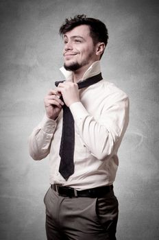 Sexy stylish businessman adjusting tie on gray background