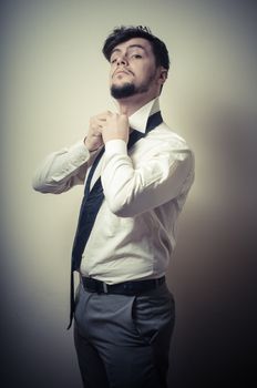 Sexy stylish businessman adjusting tie on gray background