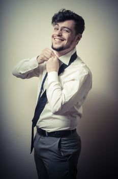 Sexy stylish businessman adjusting tie on gray background