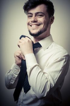 Sexy stylish businessman adjusting tie on gray background