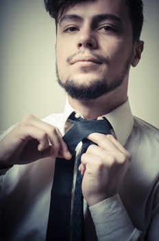 Sexy stylish businessman adjusting tie on gray background