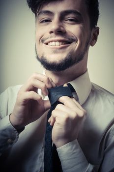 Sexy stylish businessman adjusting tie on gray background