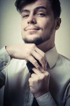 Sexy stylish businessman adjusting tie on gray background