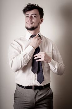 Sexy stylish businessman adjusting tie on gray background