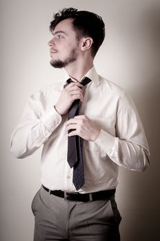 Sexy stylish businessman adjusting tie on gray background