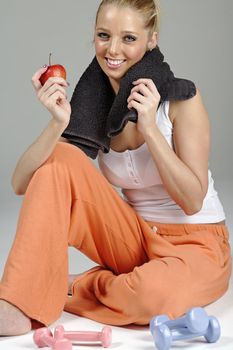 Beautiful young woman resting after exercise in fitness wear holding an apple