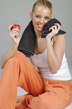 Beautiful young woman resting after exercise in fitness wear holding an apple