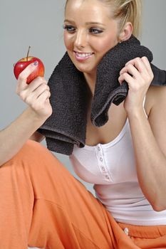 Beautiful young woman resting after exercise in fitness wear holding an apple