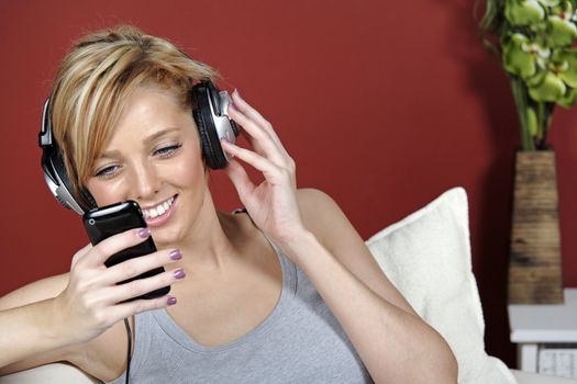 Beautiful young woman lying on sofa at home listening to music on headphones