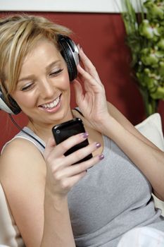 Beautiful young woman lying on sofa at home listening to music on headphones