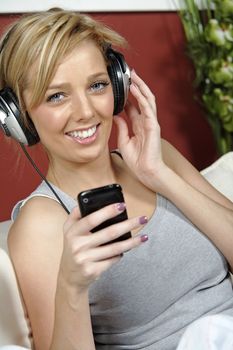 Beautiful young woman lying on sofa at home listening to music on headphones