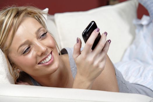 Beautiful young woman lying on sofa at home reading a text message.