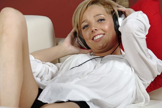 Beautiful young woman lying on sofa at home listening to music on headphones