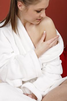 Young woman sat on her sofa at home weaing a white bath robe