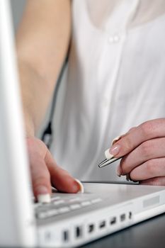 Woman using laptop while holding  pen at work