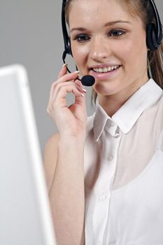 Young woman working on alptop and talking on a headset at work