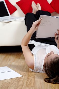 Young woman working from home reading documents while lying on the floor