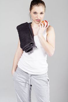 Young woman resting after exercise in fitness wear eating an apple