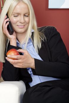 Young woman holding an apple and phone while relaxing at home