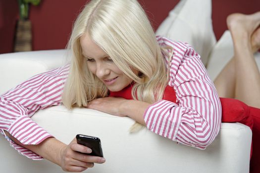 Young woman texting on her mobile phone, while resting on the sofa