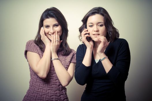 two beautiful girls gossiping on the phone on gray background