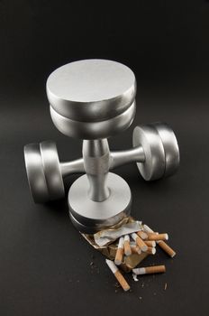 pack of cigarettes crushed metal dumbbell on a black background. Sports wins bad habits.