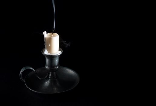 extinguished candle in an old tin candlestick and smoke on a black background