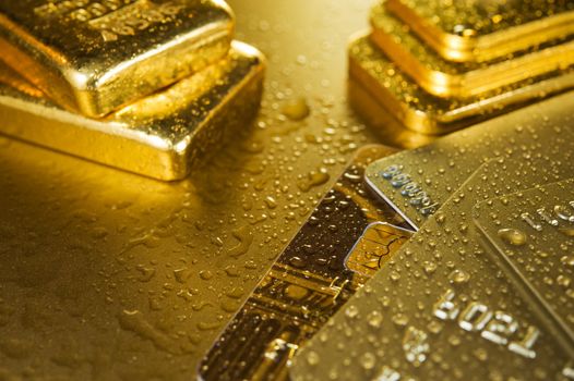 fine gold ingots and credit cards on a wet golden background