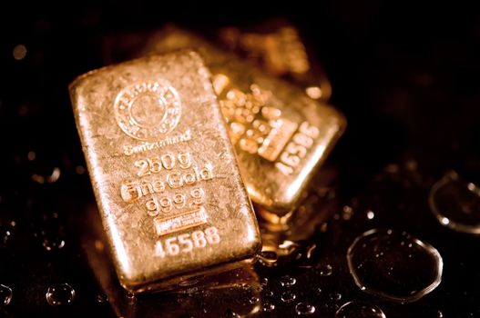 three gold ingots and water droplets on a black background. shallow depth of field.