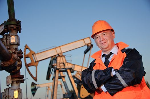 Oil worker in orange uniform and helmet on of background the pump jack and blue sky.