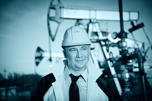 Oil worker in uniform and helmet on of background the pump jack and sky. Toned.