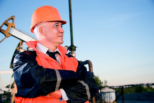 Oil worker in orange uniform and helmet on of background the pump jack and blue sky.