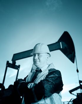 Oil worker in uniform and helmet on of background the pump jack and sky. Toned.