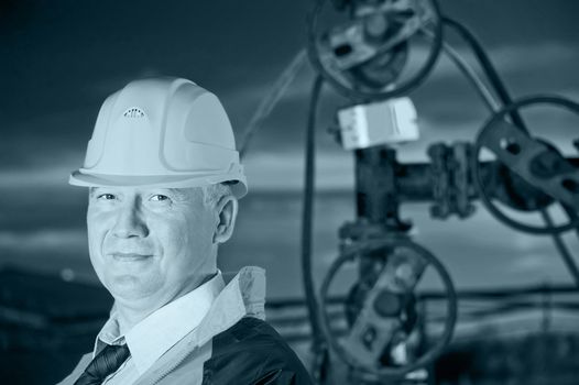 Oil worker in uniform and helmet on a background the valves, piping and sunset sky. Toned.