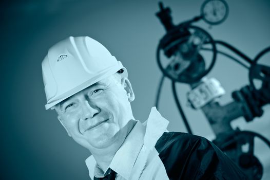 Worker in uniform and helmet on of background the valves, piping and sky. Look into the camera. Toned.